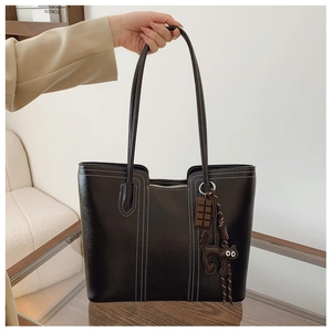 Detail of black leather tote bag with white contrast stitching and cartoon cat charm