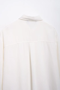 Close-up detail of the back pleats and shoulder stitching on a white crepe long sleeve shirt
