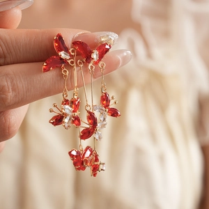 Gros plan de boucles d'oreilles papillon dorées avec zircons rouges et glands portées