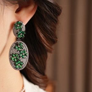 Close-up of vintage oval earrings featuring green gemstone flowers and white zircon stones