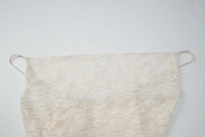 Detailed view of white lace fabric pattern and thin spaghetti straps on a slim dress