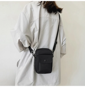 Close-up of black nylon crossbody bag with adjustable strap and front snap pocket detail