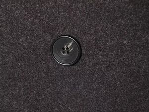 Macro shot of black four-hole button stitched on dark grey textured wool fabric detail