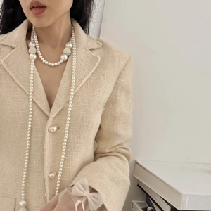 Detail of layered pearl necklace with pavé diamond spheres on a tweed jacket