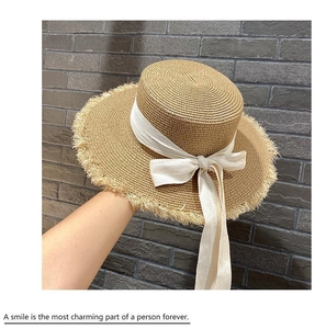 Detail of straw sun hat featuring a white ribbon bow and rustic fringed edge design