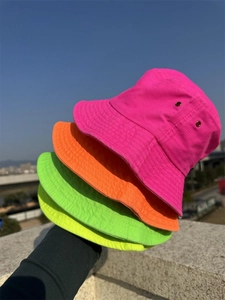 Stack of neon cotton bucket hats in rose, orange, green, and yellow under the sky