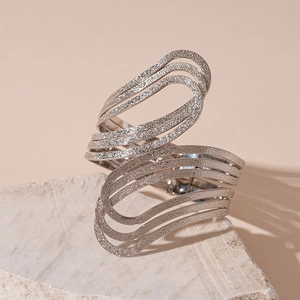 Detail of silver wavy multilayer open bangle with textured matte finish on marble
