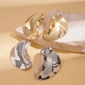 Minimalist irregular geometric metal earrings in gold and silver finishes on a stone