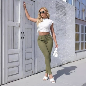 Woman in olive green high waist skinny jeans and white crop top standing by a rustic wall