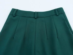 Detail shot of dark green trousers showing belt loops and pleated waist design