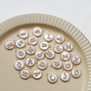Detailed view of gold-plated shell alphabet charms with zircon inlay on a ceramic plate