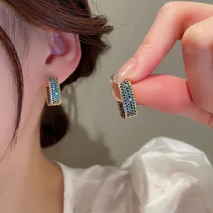 Elegant gold geometric earrings with pavé teal zircon stones shown on a model