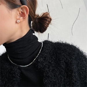 Detail of white flower stud earring and minimalist beaded necklace on a model