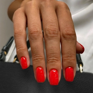 Glossy vibrant red short square false nails shown on hand with high mirror shine finish