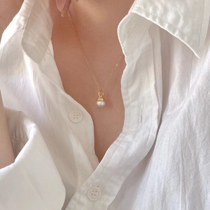 Close-up of minimalist gold pearl necklace worn on a classic white shirt collar