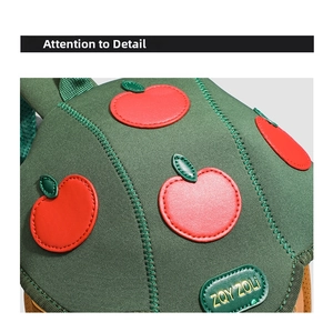 Detailed view of green kids backpack featuring red apple embroidery and fine stitching