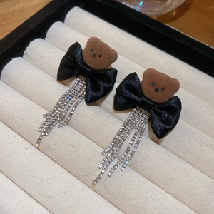 Detail of bear stud earring with black bow and sparkling rhinestone tassels on beige velvet