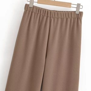 Detail of brown wide-leg trousers with elastic waistband and textured fabric on wooden hanger