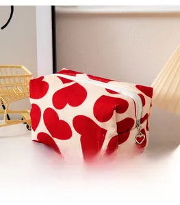 Detail of beige canvas makeup bag featuring red heart patterns and heart-shaped metal zipper