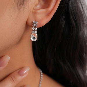 Close-up of silver dangle earring featuring emerald-cut crystals and round zircons