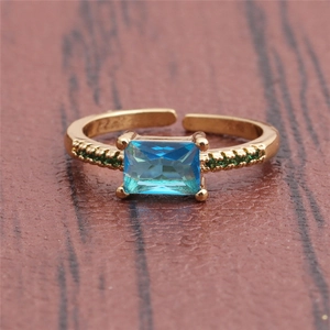 Close-up of golden ring with rectangle blue gemstone and small green side stones