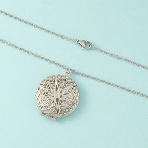 Vue macro d'un médaillon rond en acier 316L avec motif floral évidé et charnière