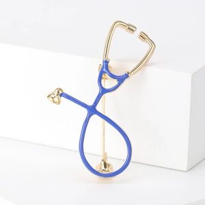 Detail of a golden stethoscope brooch with blue enamel inlay on a white pedestal