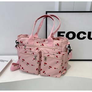Detailed view of pink tote bag featuring a cherry print and multiple front zipper pockets