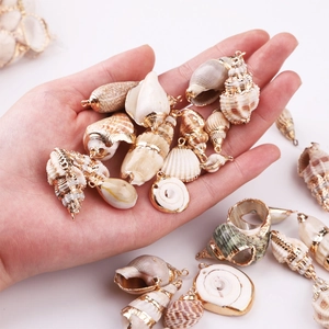 Hand holding assorted natural seashell pendants with gold plated edges for DIY jewelry