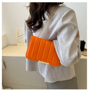 Detail of orange quilted shoulder bag with gold chain strap and metal trim on model