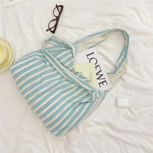 Detail of blue and white striped canvas tote bag on a bed with daily lifestyle accessories