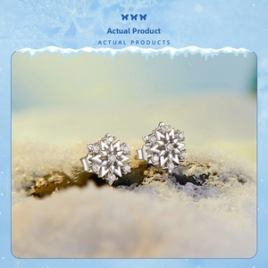 Macro view of snowflake stud earrings featuring white zircons on a winter snow background