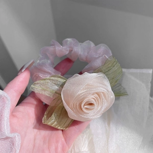 Close-up of soft pink organza rose scrunchie with green leaf detail held in hand