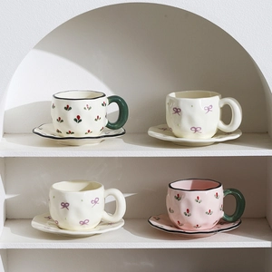 Handmade ceramic coffee cup and saucer set with floral and bow patterns on white shelf