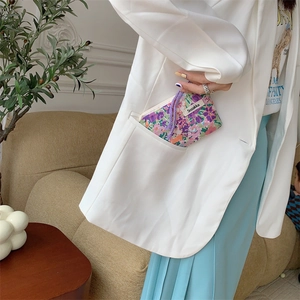 Floral fabric pouch with purple drawstring being placed into a blazer pocket