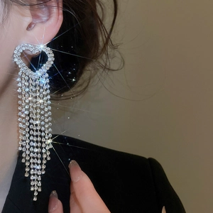 Detailed view of silver heart tassel earrings with sparkling rhinestones on model