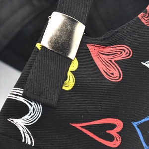 Close-up of black baseball cap featuring colorful graffiti heart prints and metal buckle