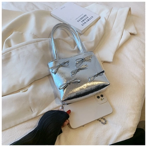 Detail of silver metallic handbag featuring 3D bow accents on a beige bedding background