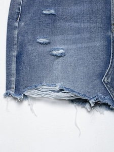Close-up of distressed denim shorts featuring ripped holes and frayed hemline detail