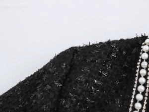 Detail eines Tweedkleides mit Perlen und Strasssteinen auf schwarzem Stoffbesatz