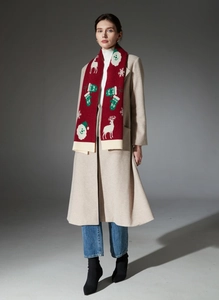 Detail of red Christmas scarf with reindeer patterns worn over a beige winter coat
