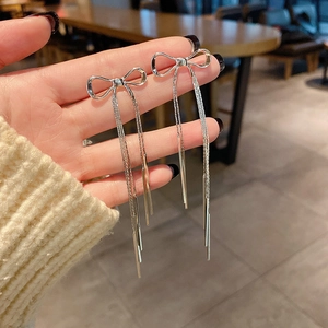 Detailed close-up of silver bow tassel earrings with long metallic fringe held in hand