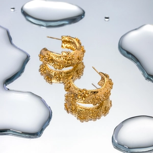 Macro detail of 18k gold plated hammered floral C-shape earrings on water drops mirror