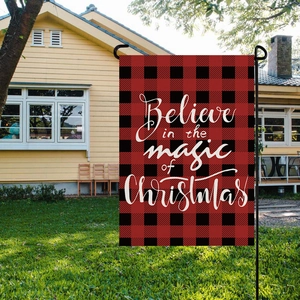 Outdoor scene of a red buffalo plaid Christmas garden flag on a lawn with house background
