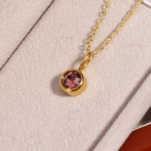 Macro detail of gold birthstone necklace with pink round crystal in beige velvet jewelry box