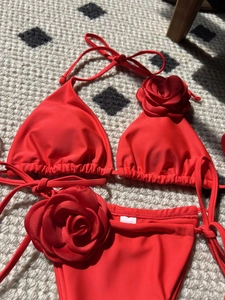 Flat lay of bright red bikini featuring large 3D rose flower decorations and side ties