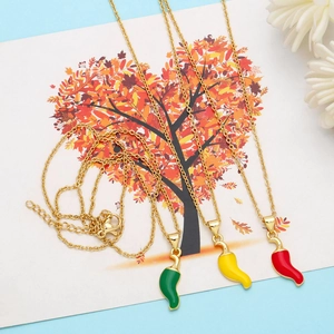 Close-up of three enamel chili pendants in green, yellow and red on golden chains