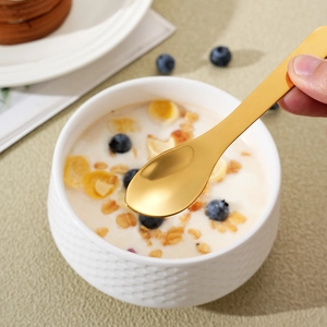 Golden stainless steel dessert spoon held over a breakfast bowl with yogurt and blueberries