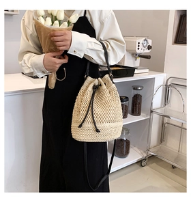 Straw bucket bag detail with black PU leather straps shown on model in a casual setting