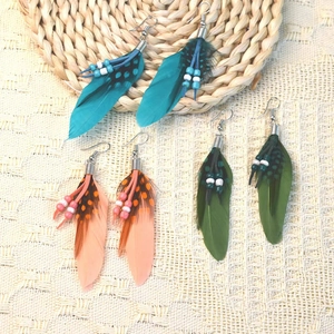 Detailed macro view of bohemian peacock blue, coral, and olive green feather earrings